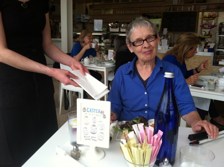 A waitress is holding out a napkin to a woman who seems unaware of it. There is a folded white cane on the edge of the table. 
